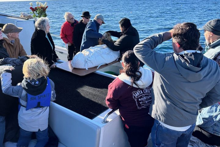 People gathered on a boat for a ceremony, with flowers and the ocean in the background.