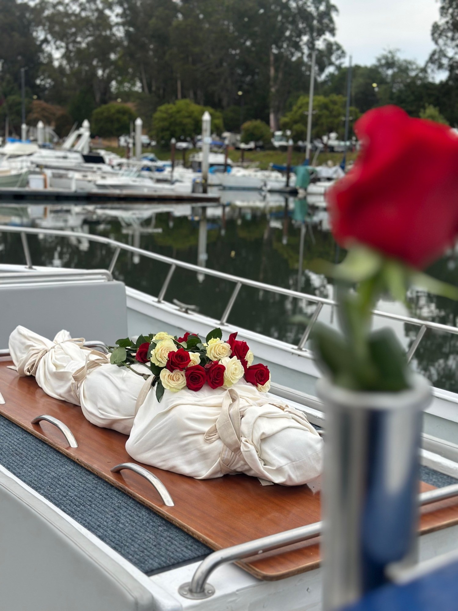 Wrapped body with roses on a boat deck, blurred marina in background.