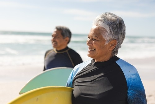Two smiling surfers with boards on a sunny beach.