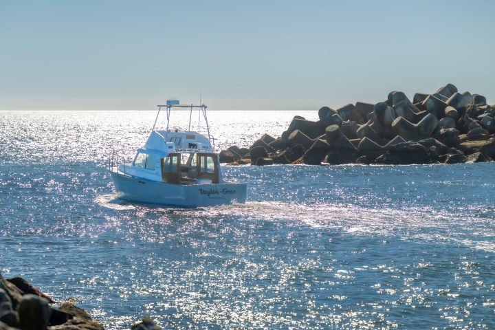 Boat sailing in sunny sea near rocky breakwater.