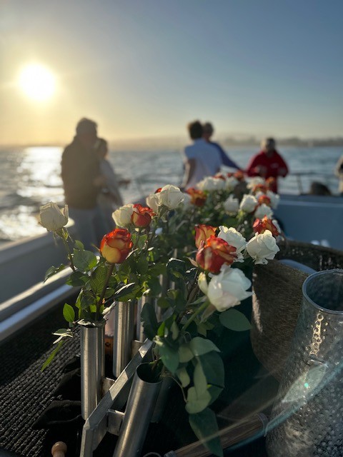Roses in vases on a boat at sunset with people in the background.