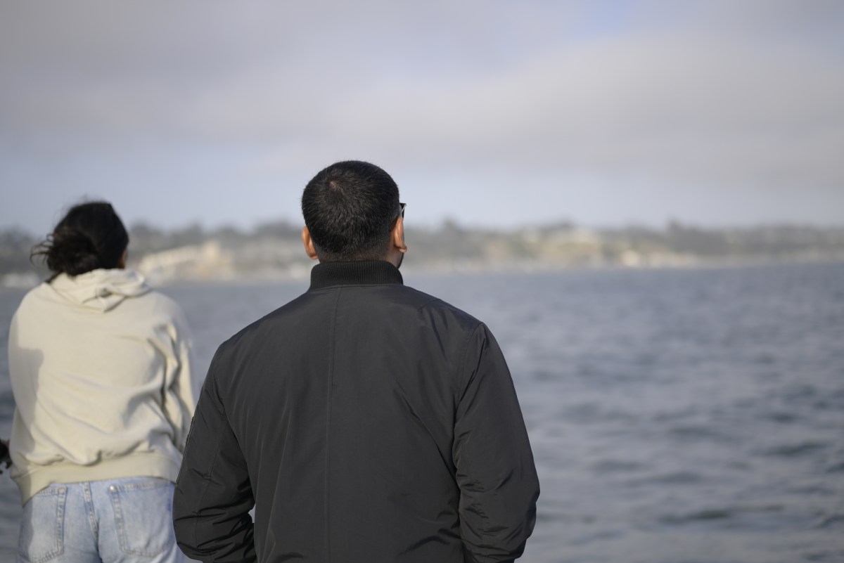 Two people facing a body of water under a cloudy sky.